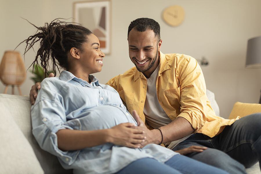 Happy african american couple expecting baby, pregnant black spouses embracing on couch at home