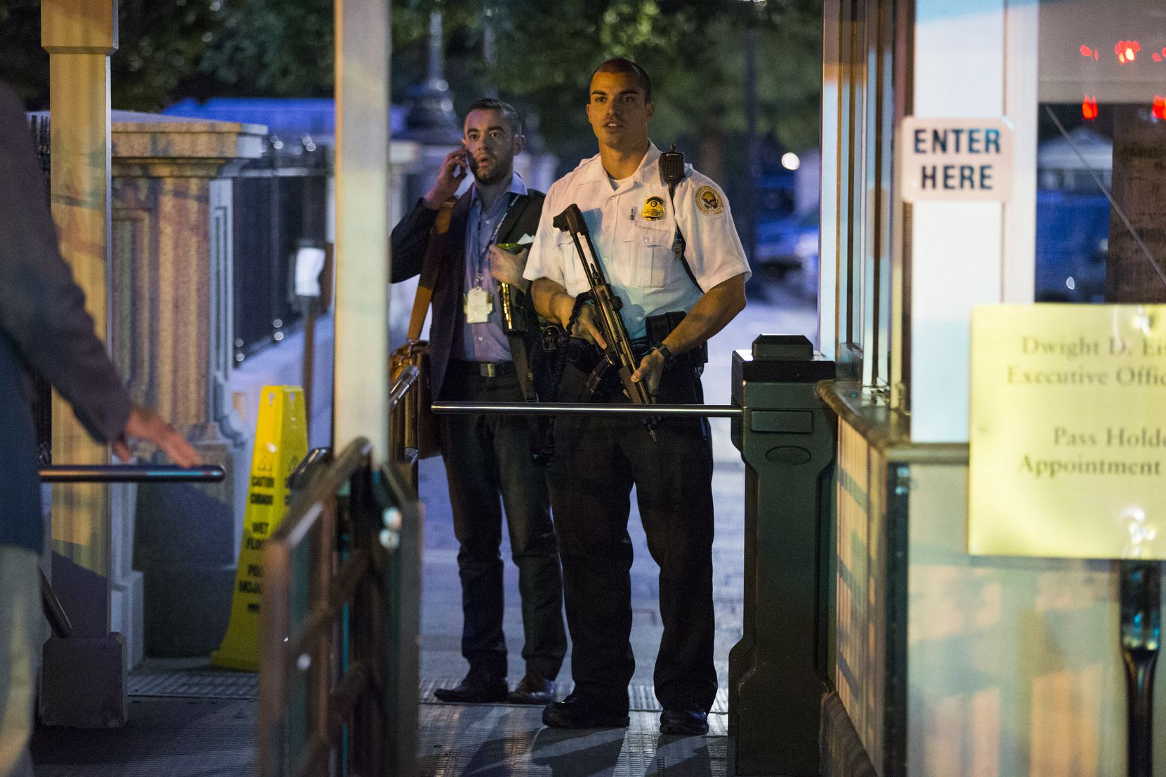 A Secret Service police officer holds a weapon as he stands near an entrance to the White...