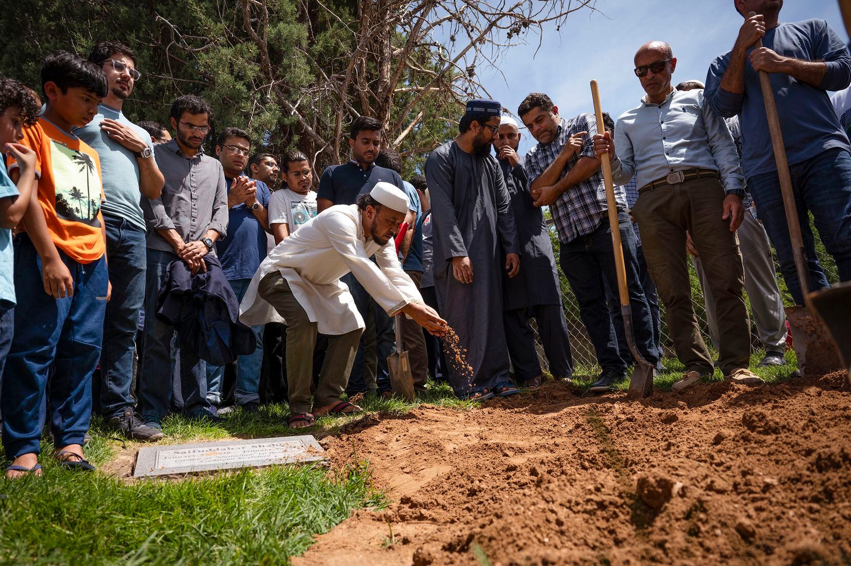 People sprinkle dirt over the grave of Muhammad Afzaal Hussain, 27, at Fairview Memorial...