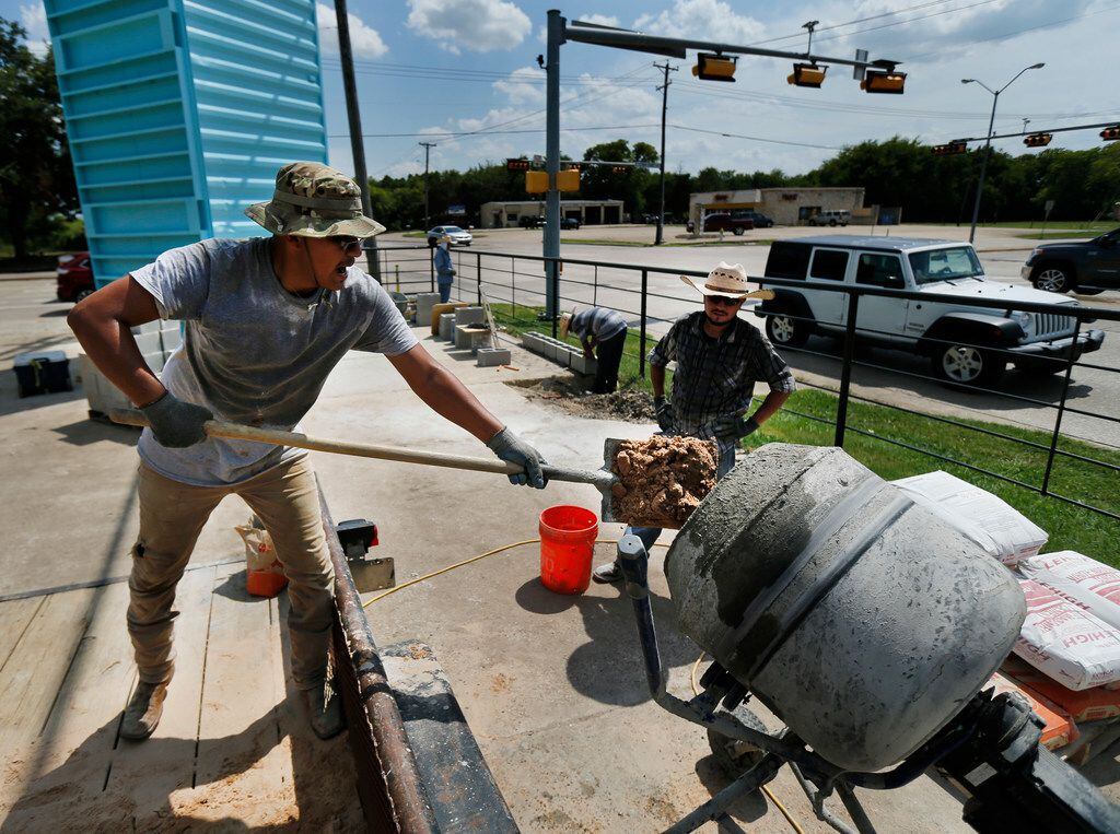 Construction worker Jesse Hernandez shovels sand into a mixer as he and a crew build a...