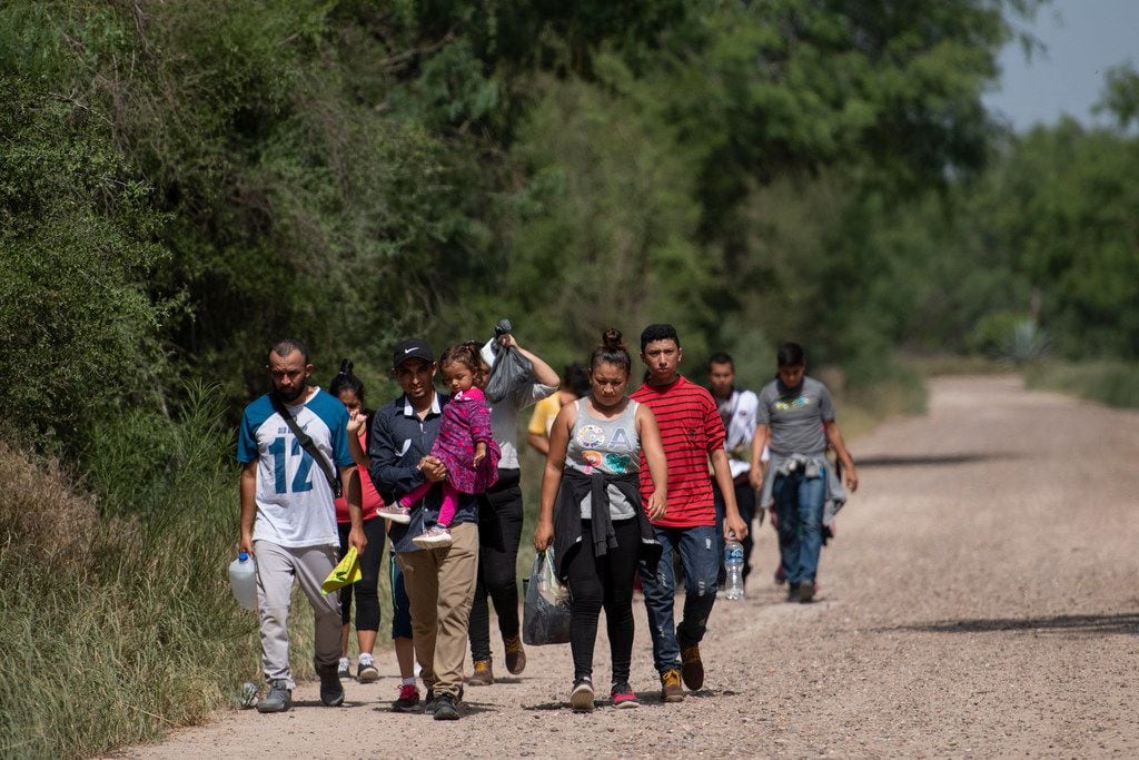 Hours after officials toured the border area of South Texas, migrant families walk toward...