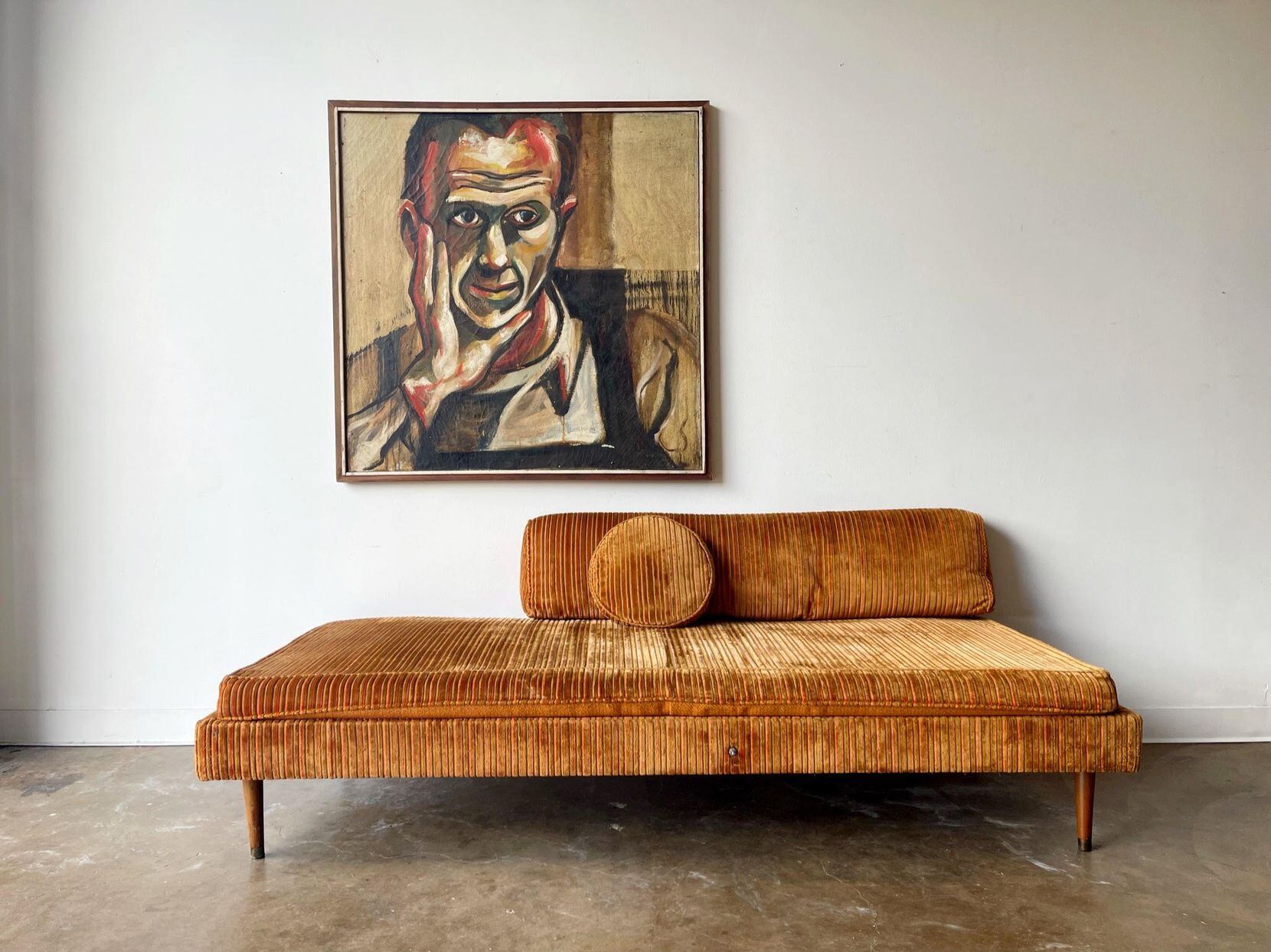 A painting hangs behind a chaise lounge couch.