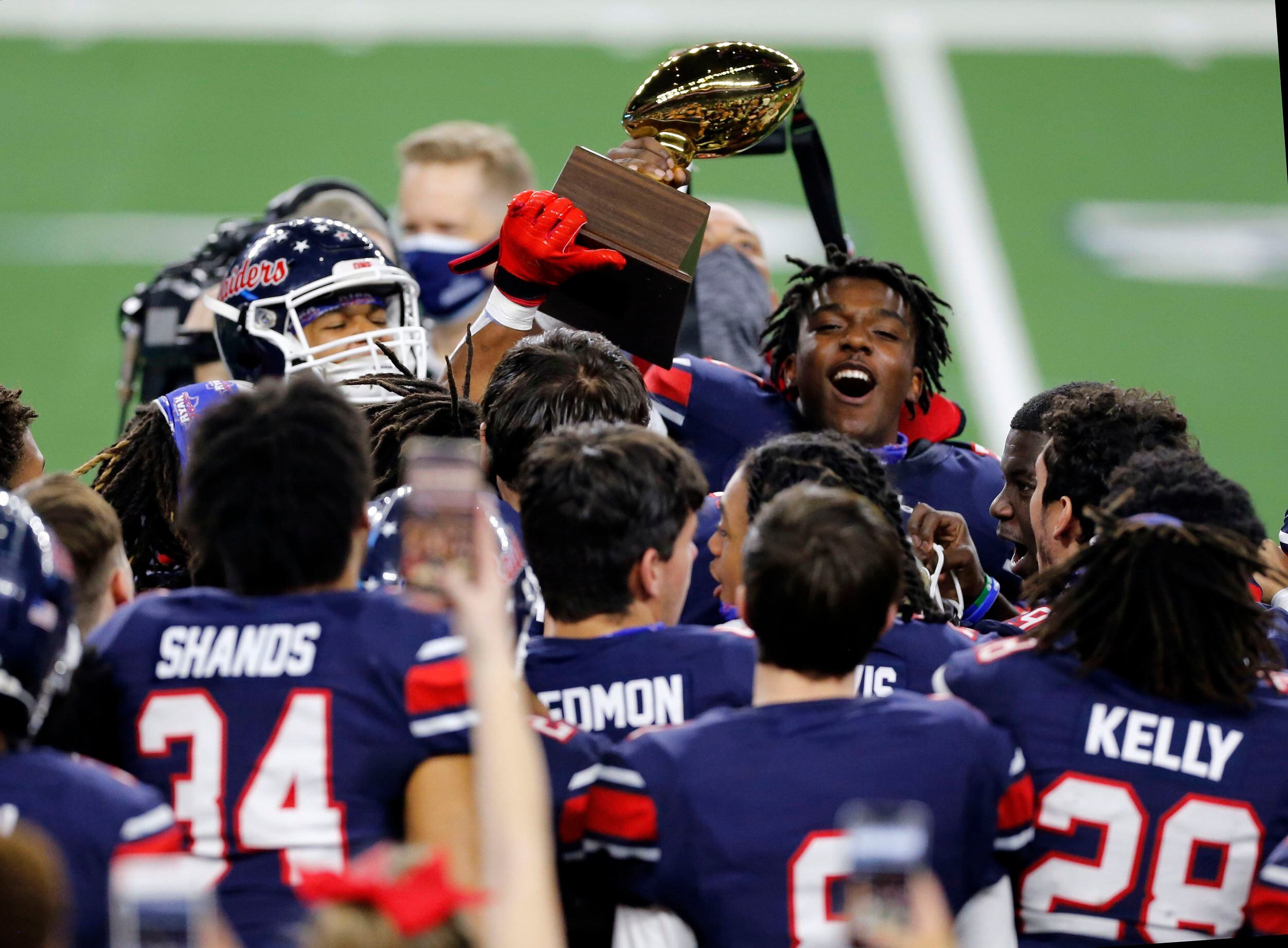 Members of the Denton Ryan football team celebrate with the trophy after winning the Class...