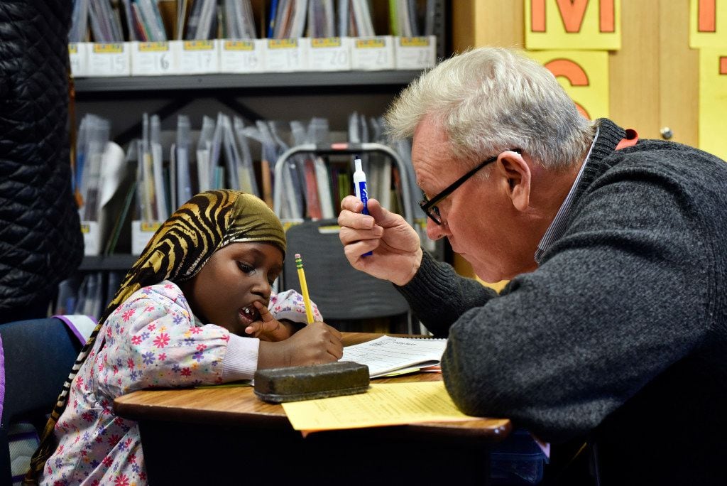 First grader Halima Hassan works with volunteer Gerald Fogarty on English spelling and...