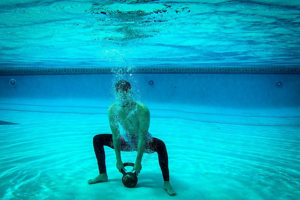 Texas Rangers pitcher Alex Claudio does squats underwater while holding a kettlebell during...