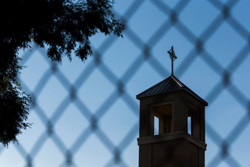 The steeple is seen through a fence outside of St. Cecilia Catholic Church during an evening...