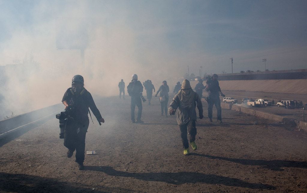 Migrants run from tear gas launched by U.S. agents, amid photojournalists covering the...