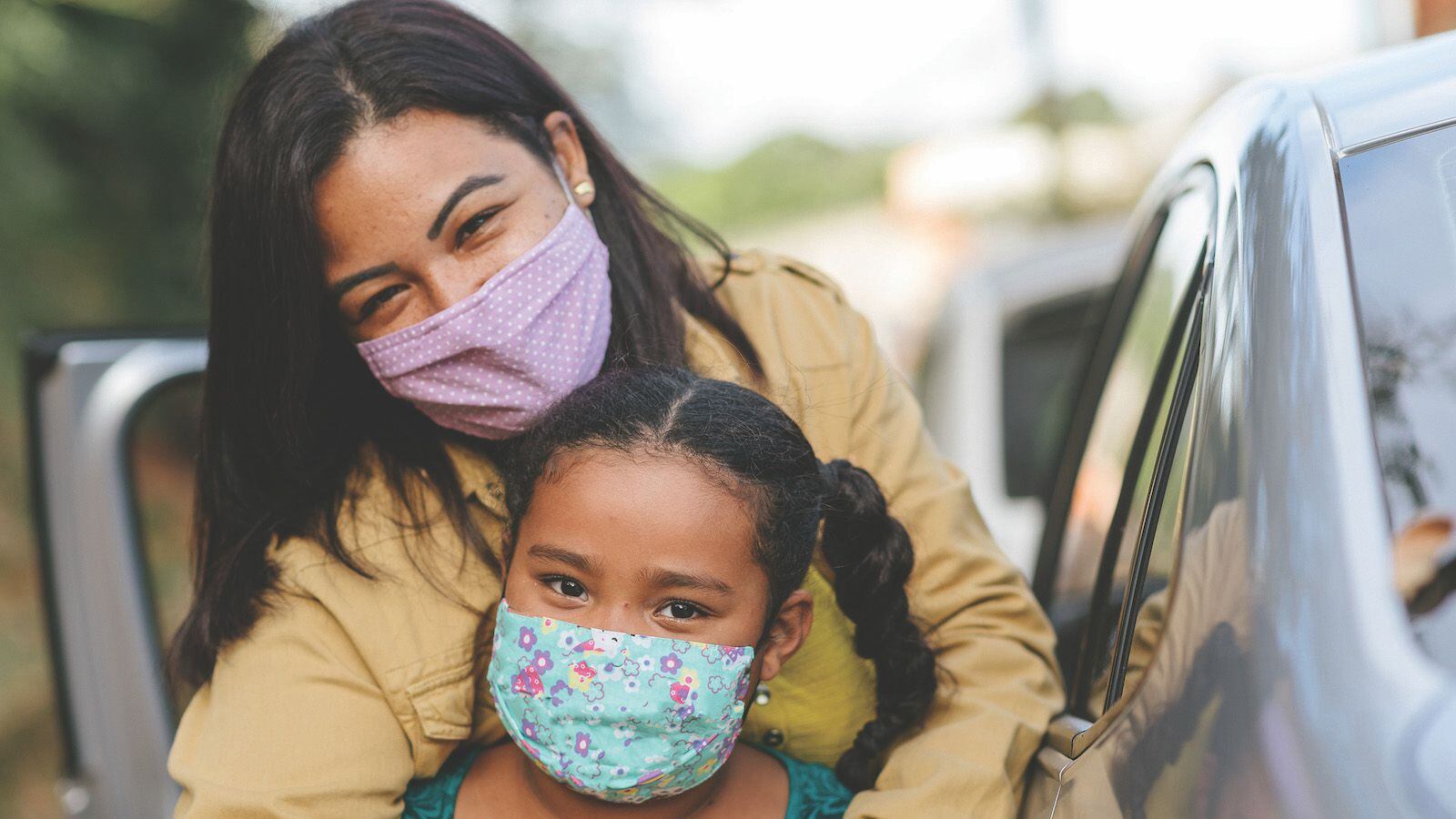 Una madre e hija feliz con máscaras faciales y junto a un coche.