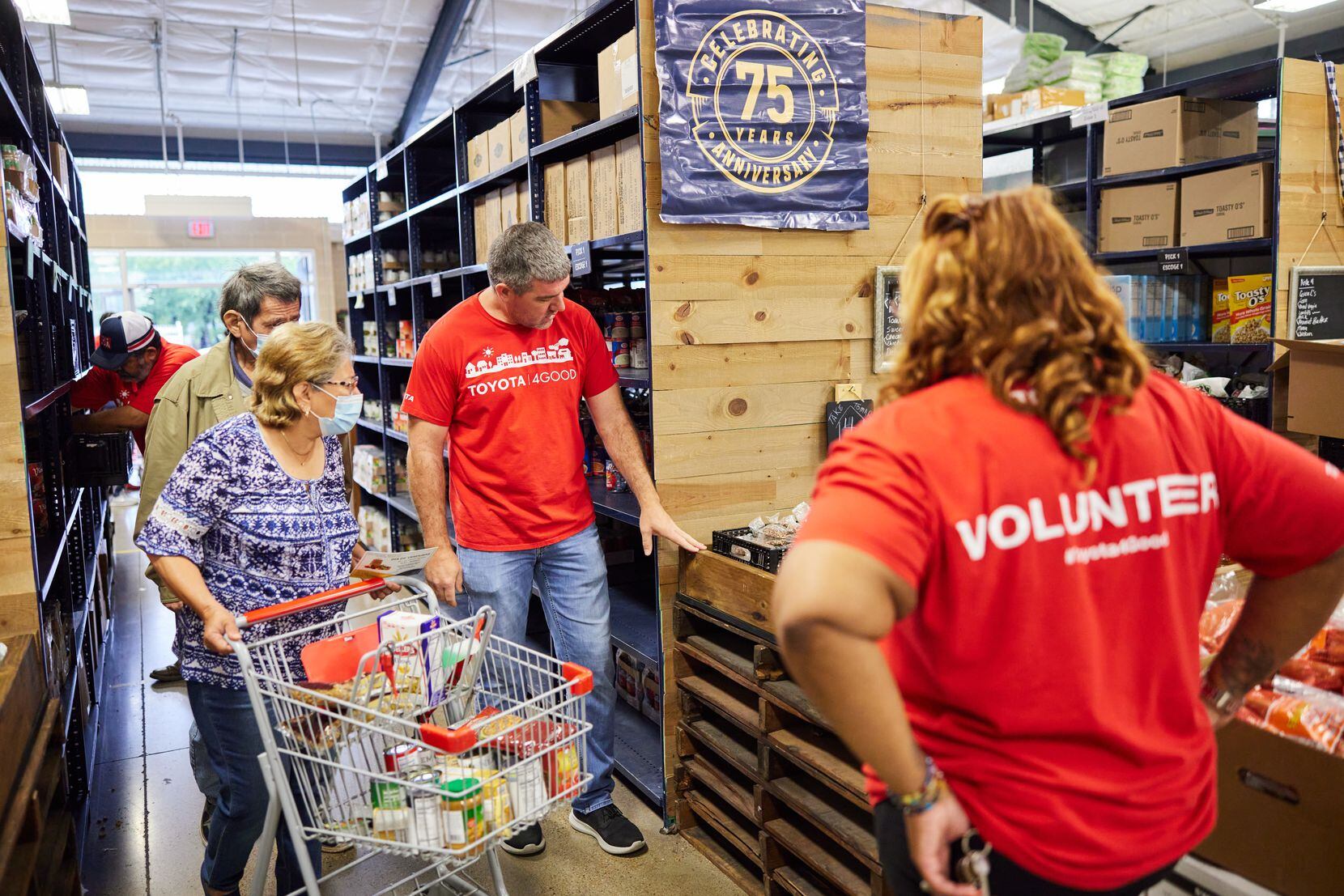 Volunteers in red T-shirts help woman pushing grocery cart through food pantry.