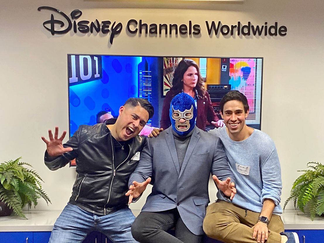 Foto de  Blue Demon Jr enseguida de dos actores enfrente de un anuncio que dice "Disney...