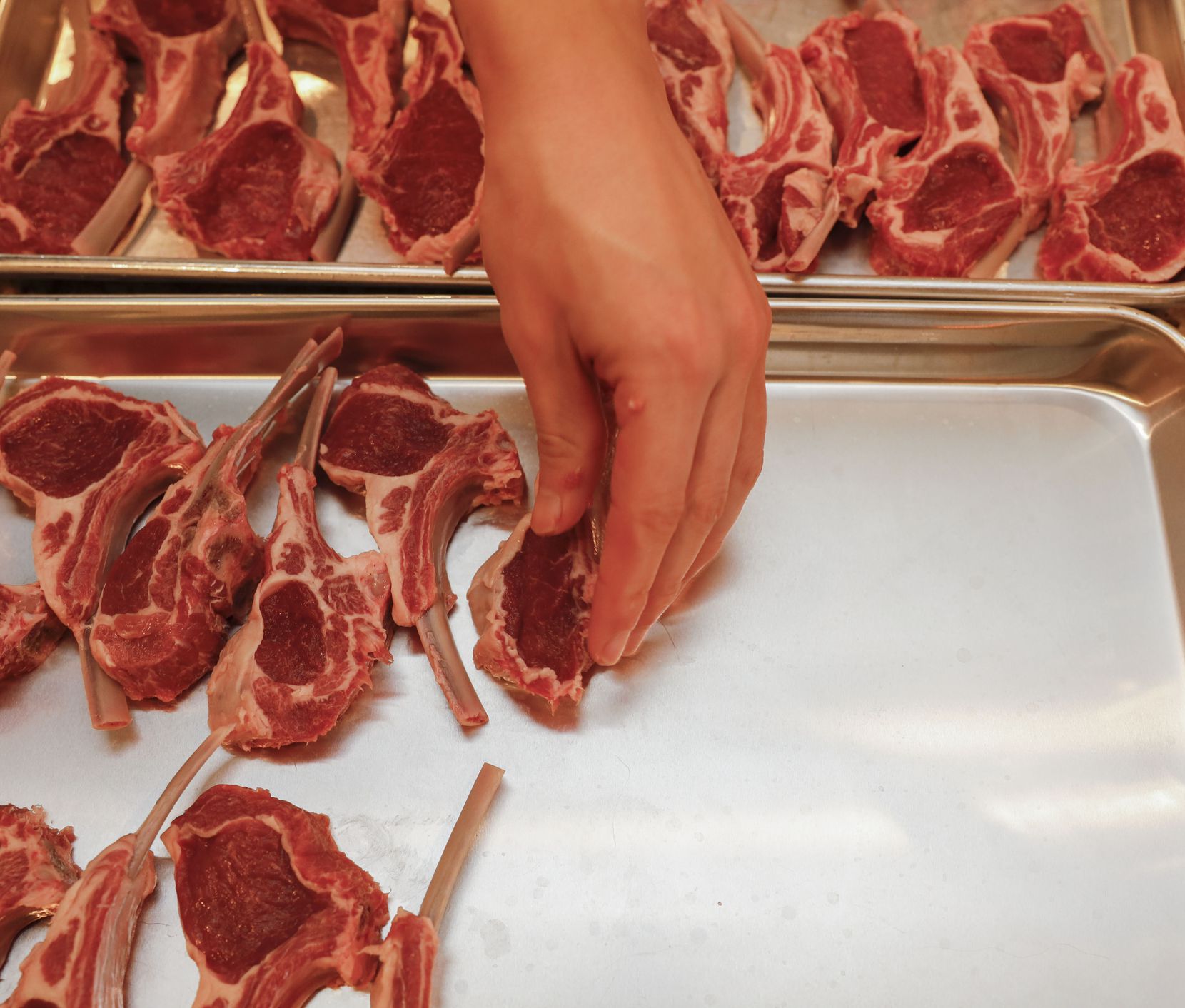 Preston Nguyen puts cut lamb chops on a tray while preparing a catering order at his home in...