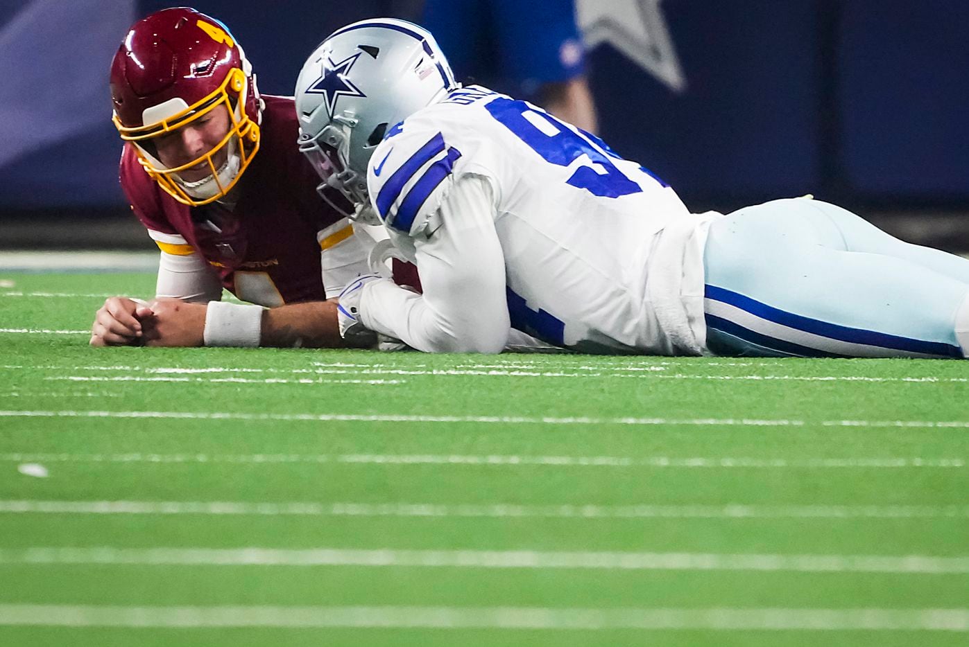 Dallas Cowboys defensive end Randy Gregory (94) lies on the ground and talks with Washington Football Team quarterback Taylor Heinicke (4) during the first half of an NFL football game at AT&T Stadium on Sunday, Dec. 26, 2021, in Arlington.