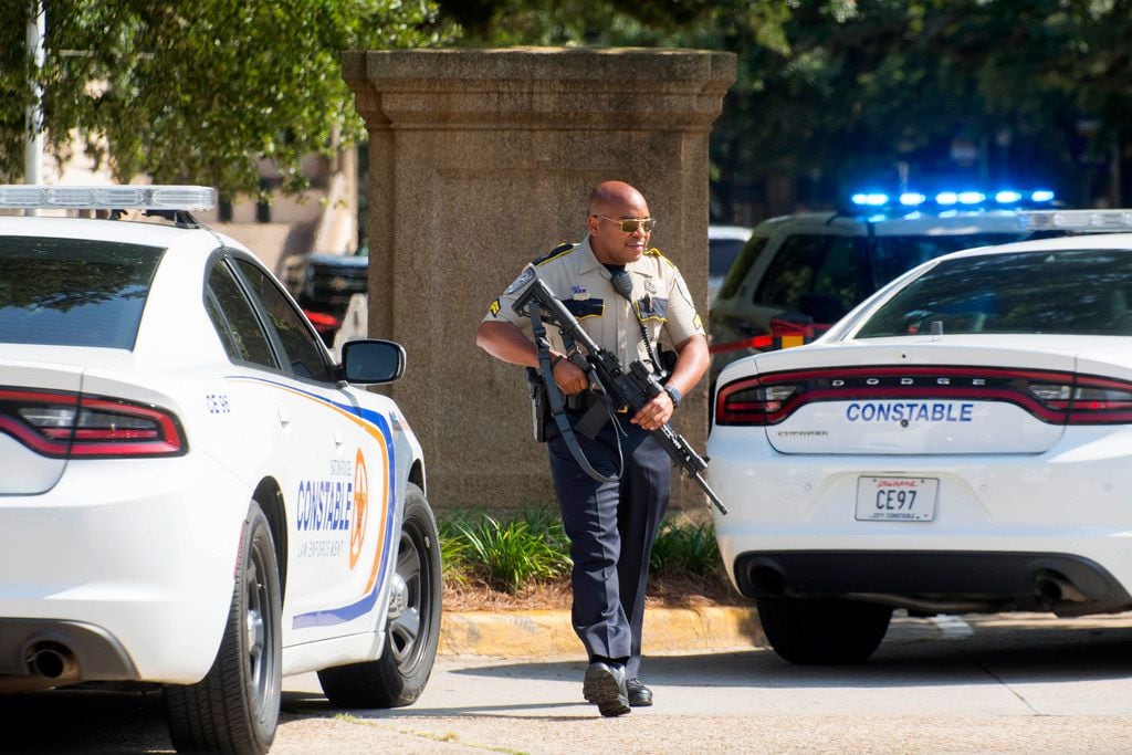 A Baton Rouge City Constable's Office officer with a weapon walks near two LSU police...