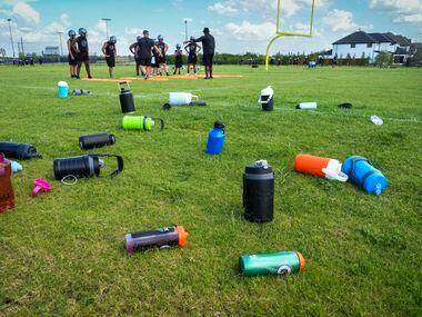 Water bottles rest on the field as players run drills during the first day of football...