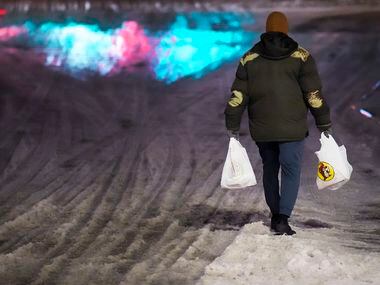 A customer carries bags through snow and ice as he walks away after making a purchase at...
