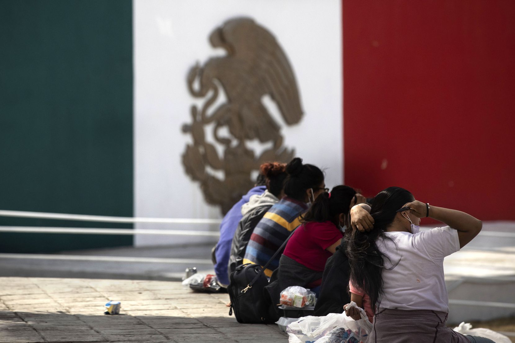 A migrant woman brushed her hair as she and other expelled migrants sat at a plaza near the...