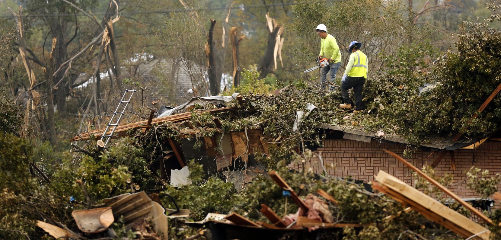 Workers cut up and remove a tree that toppled onto a home on Royal Lane in northwest Dallas.